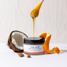 Load image into Gallery viewer, Jar of 'Fur Love' product with honey being drizzled over it, surrounded by a coconut, almonds, and an orange peel on a white background.