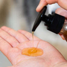 Load image into Gallery viewer, Hand holding a bottle pouring orange manuka honey Fur Love natural dog shampoo into another hand